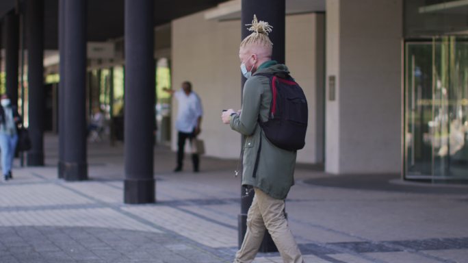白化病非裔美国人，戴着口罩，留着长发绺，走路用智能手机