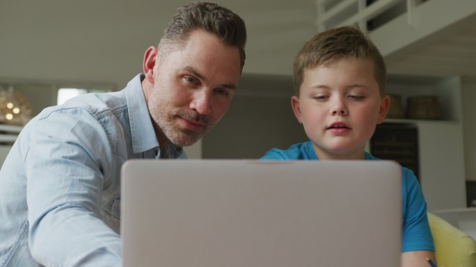 白人父亲带着儿子坐在家里用笔记本电脑学习