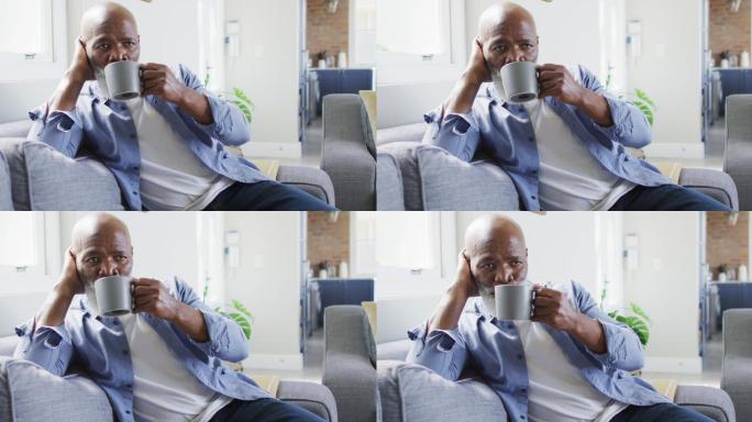 深思熟虑的非洲裔美国人坐在客厅的沙发上，喝着咖啡