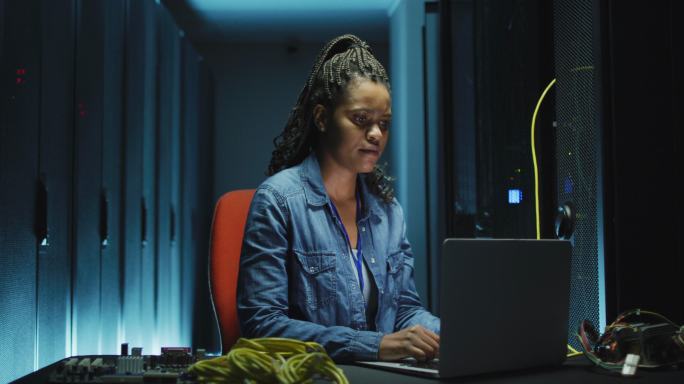 非裔美国女性计算机技术人员使用笔记本电脑在企业服务器室工作
