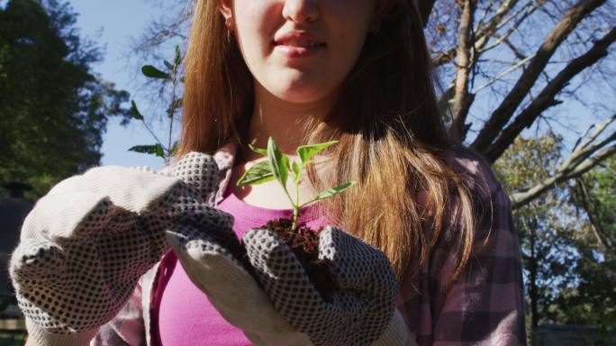 面带微笑的白人少女戴着手套在花园里工作，检查植物