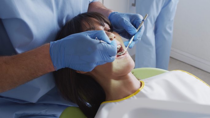 白人男性牙医和牙科护士在现代牙科诊所检查女性病人的牙齿