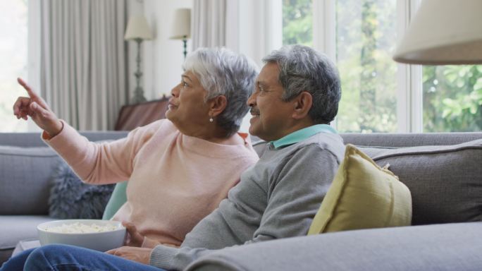 快乐的黑白混血老夫妇一边吃着爆米花一边看电视，在家里玩得很开心