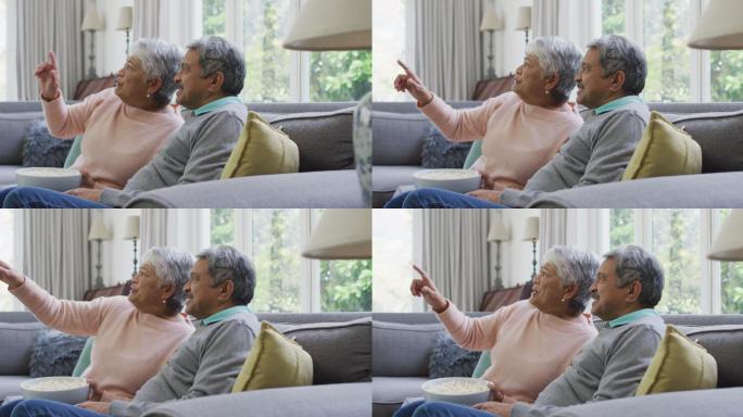 快乐的黑白混血老夫妇一边吃着爆米花一边看电视，在家里玩得很开心