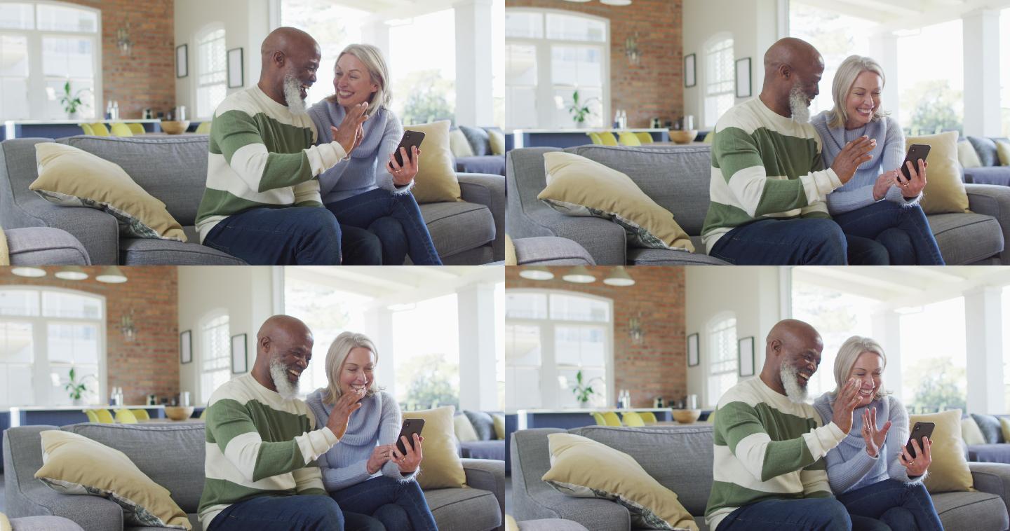 快乐的高级多样化夫妇坐在客厅的沙发上，用智能手机，视频通话