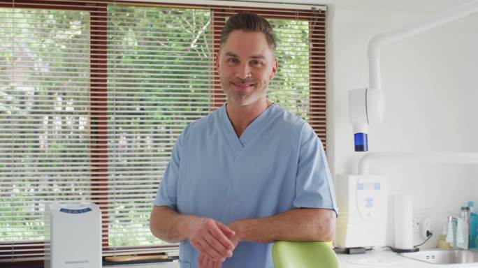 微笑的白人男性牙医的肖像看着镜头在现代牙科诊所