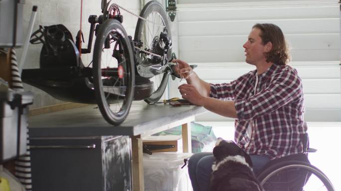 重点高加索残疾人在轮椅修理自行车在车库