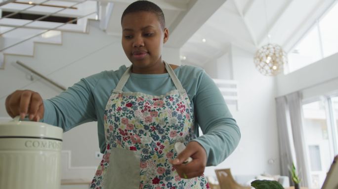 快乐的非裔美国胖女人穿着围裙，在厨房里用蔬菜垃圾堆肥做饭