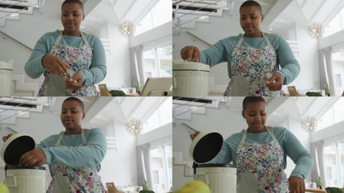 快乐的非裔美国胖女人穿着围裙，在厨房里用蔬菜垃圾堆肥做饭