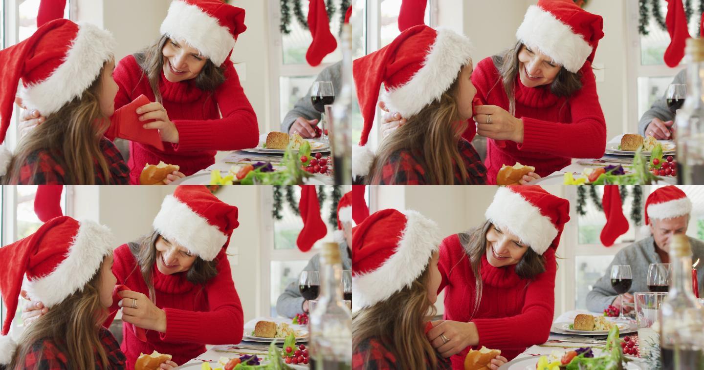 快乐的白人母亲在圣诞餐桌上给女儿擦嘴