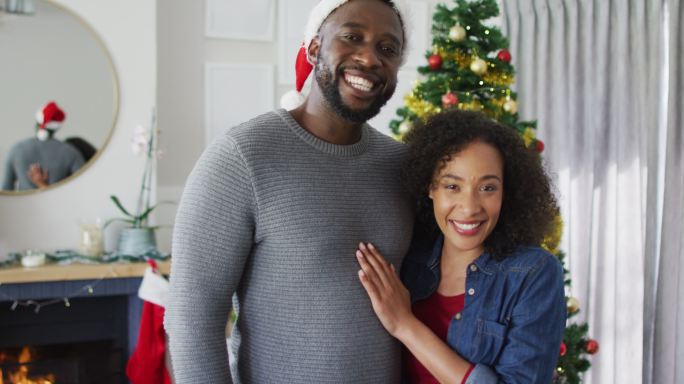 快乐的非裔美国夫妇拥抱着，看着镜头，背景是圣诞装饰