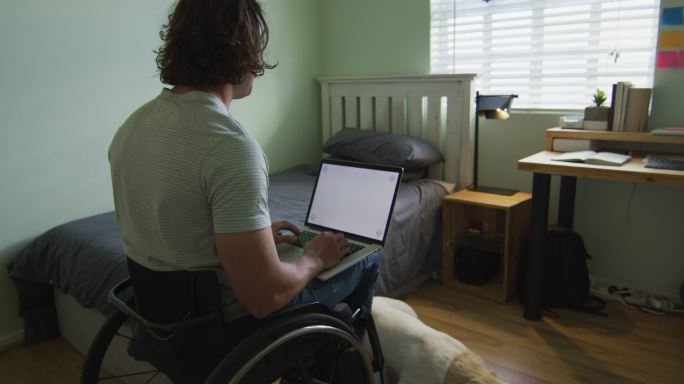 白人残疾人坐在轮椅上在卧室里使用笔记本电脑