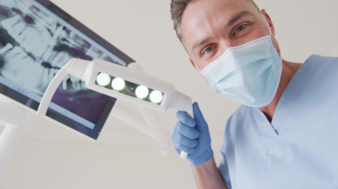 白人男性牙医带着口罩在现代牙科诊所检查牙齿