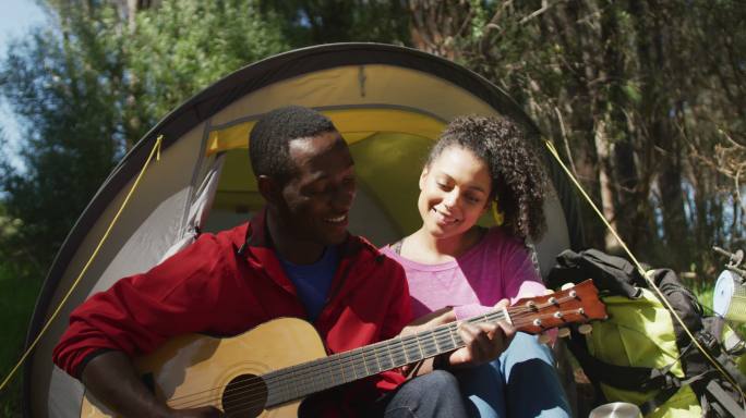 微笑的夫妇坐在帐篷和吉他在乡下