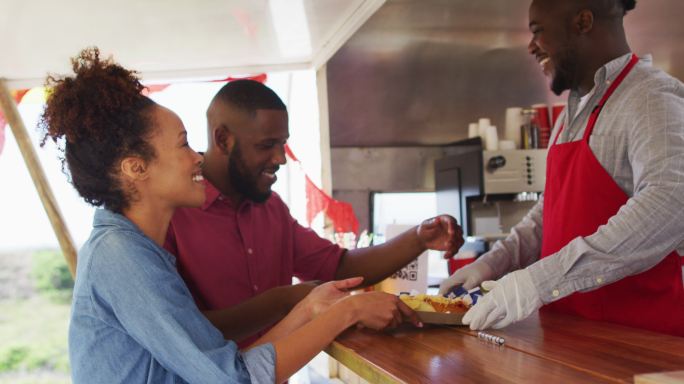面带微笑的非洲裔美国男性餐车主人为快乐的多样化夫妇提供食物