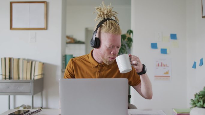 白化病非裔美国人留着脏辫喝咖啡用笔记本电脑进行视频通话