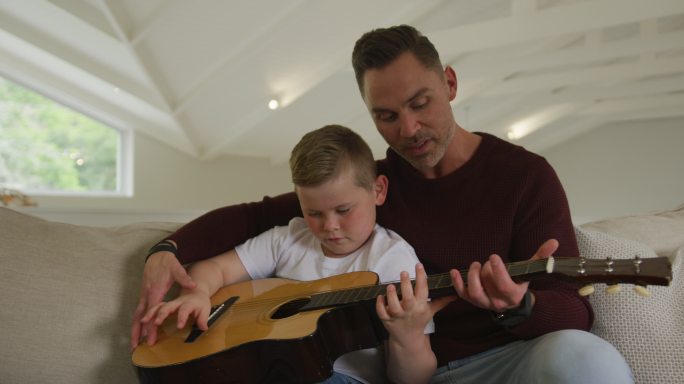 白人父亲和儿子一起坐在客厅弹吉他