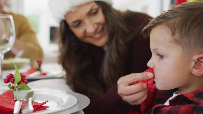 快乐的白人母亲在圣诞餐桌上给儿子擦嘴