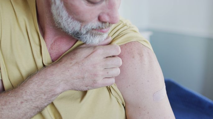 快乐的高加索成熟男子，手臂上的石膏显示他接种了冠状病毒疫苗