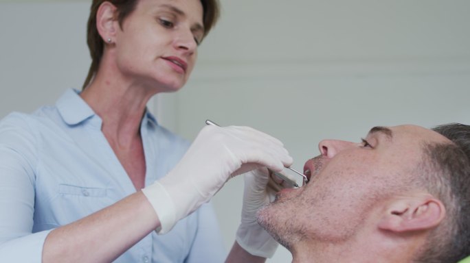 白人女牙科护士在现代牙科诊所检查男性病人的牙齿