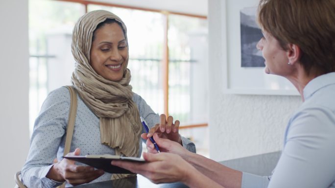 一个面带微笑的混血儿女人在现代牙科诊所的接待处交谈和签署文件
