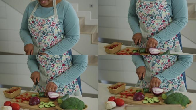 快乐的非裔美国胖女人穿着围裙，在厨房做饭，切菜