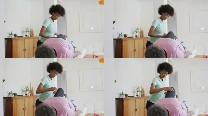 快乐的非裔美国女性理疗师帮助老年女性患者在家锻炼
