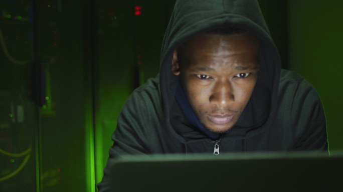 非裔美国男性电脑黑客在商业服务器室使用笔记本电脑