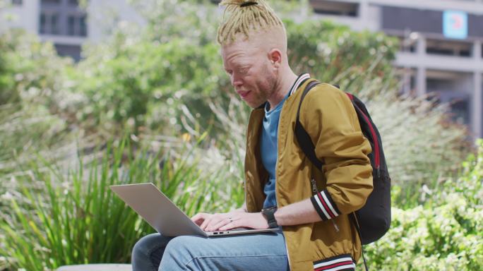 有思想的白化非裔美国人，留着脏辫，坐在公园里用笔记本电脑