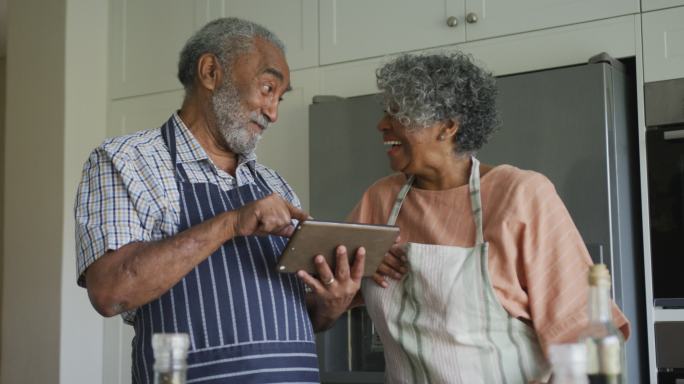 快乐的非裔美国老年夫妇一起烹饪，用平板电脑