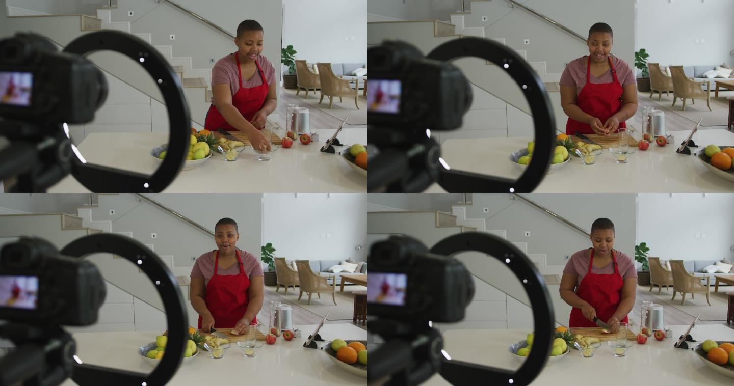 快乐的非裔美国胖女人穿着围裙，在厨房用相机制作烹饪视频博客