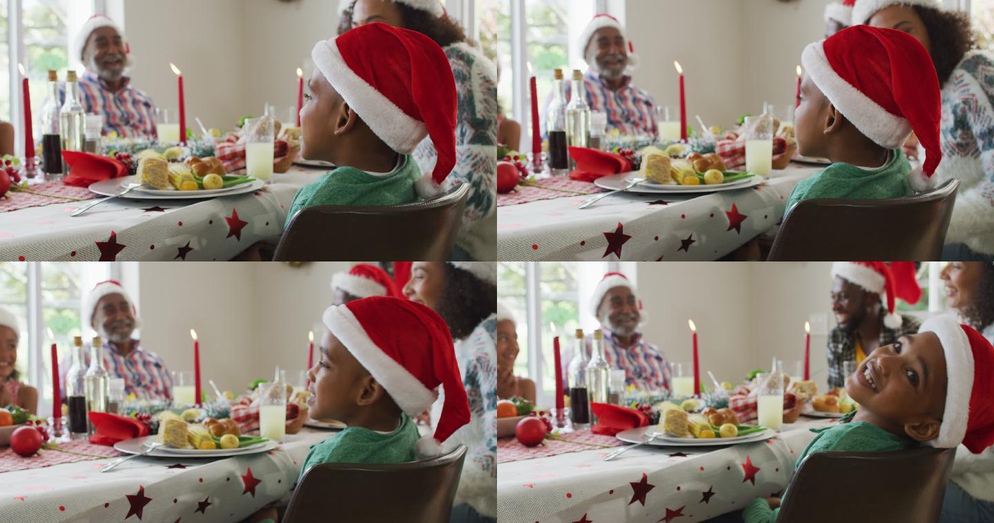 微笑的非裔美国男孩的肖像，戴着圣诞老人的帽子与家人庆祝节日大餐