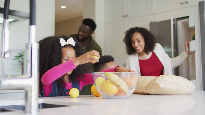 快乐的非裔美国女孩在厨房里和父母兄弟一起收拾东西