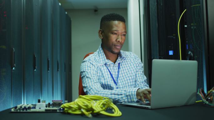 非裔美国男性电脑技术人员笔记本电脑在商业服务器室工作