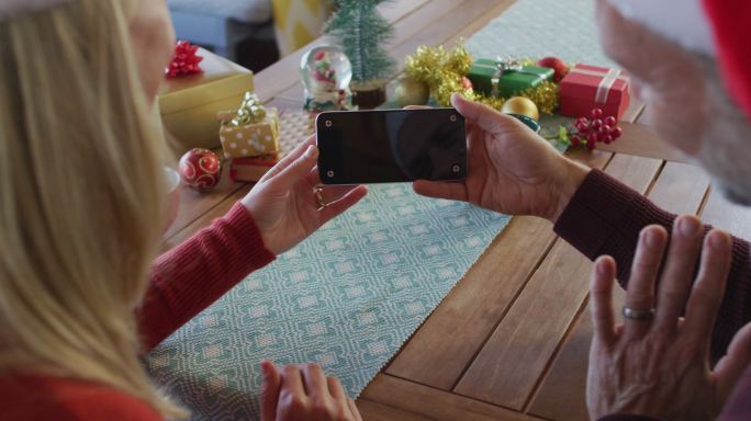 幸福的白种人成熟夫妇戴着圣诞帽，用智能手机拷贝空间