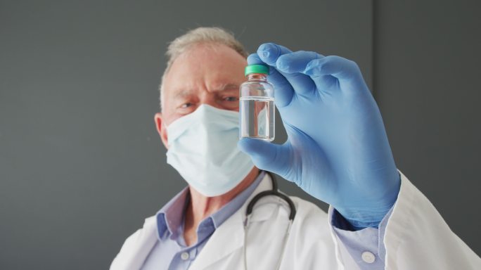 白人男医生戴着口罩手持新冠疫苗