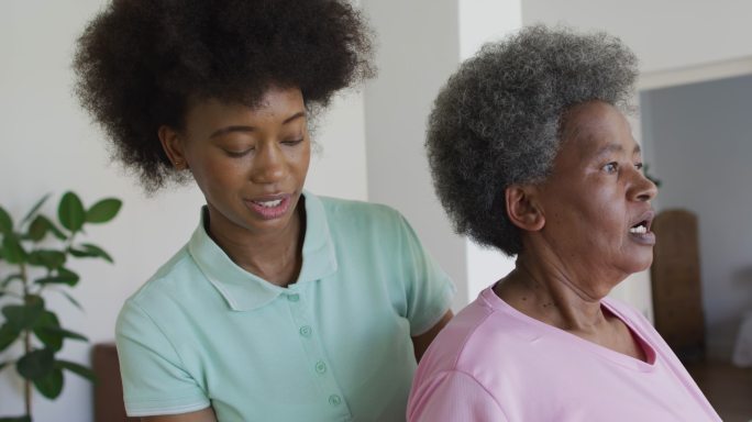 快乐的非裔美国女性理疗师帮助老年女性患者在家锻炼