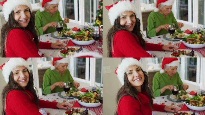 快乐的白人妇女戴着圣诞老人的帽子看着相机在圣诞大餐