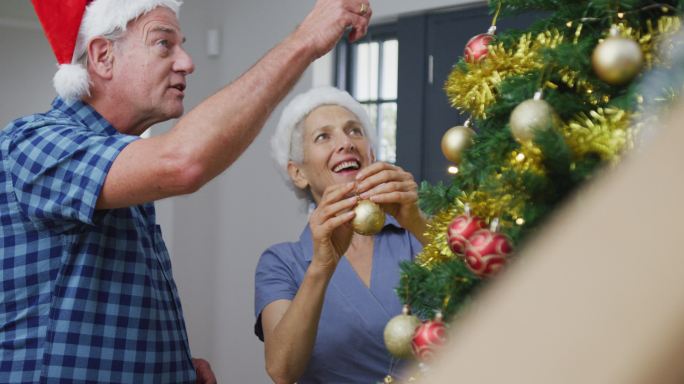 快乐的白种人老夫妇戴着圣诞帽装饰圣诞树