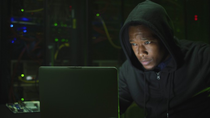 非裔美国男性电脑黑客在商业服务器室使用笔记本电脑