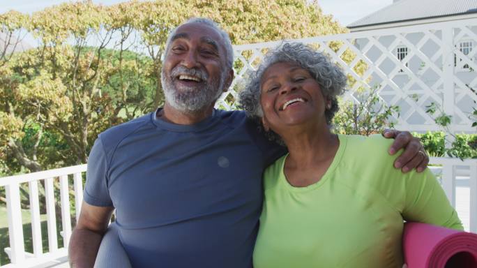 快乐的非裔美国老夫妇拿着瑜伽垫在露台上