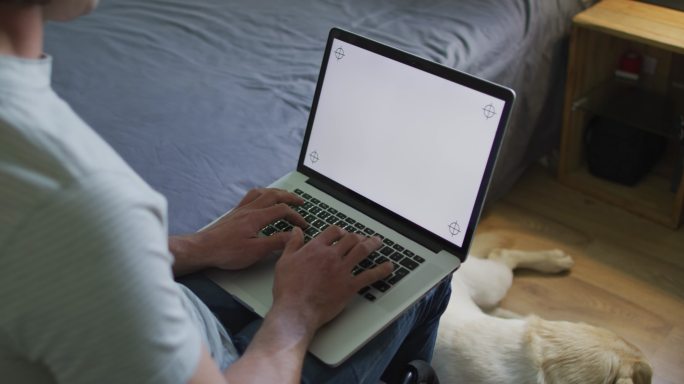 白人男子在卧室用笔记本电脑和宠物狗