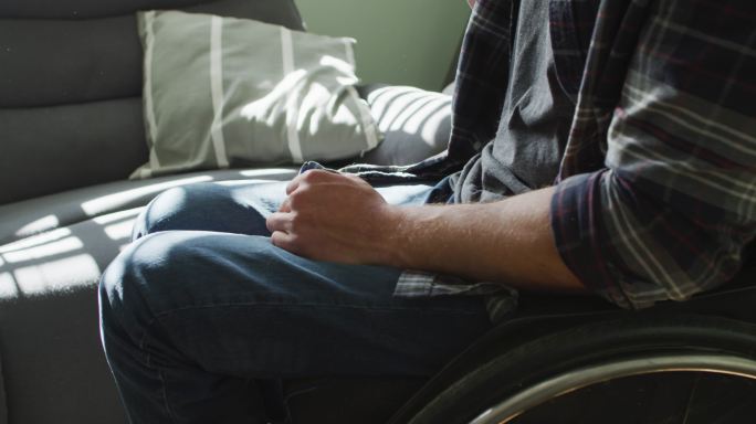 坐在轮椅上的白人残疾人在客厅里拿着一杯咖啡