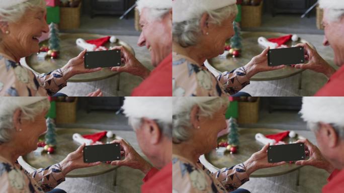 白种人老夫妇在圣诞节期间戴着圣诞老人的帽子在智能手机上进行视频通话