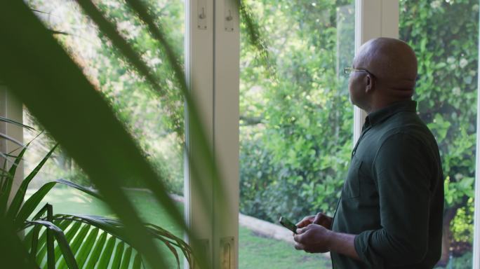 非洲裔美国老人在家里一边看窗外一边用智能手机