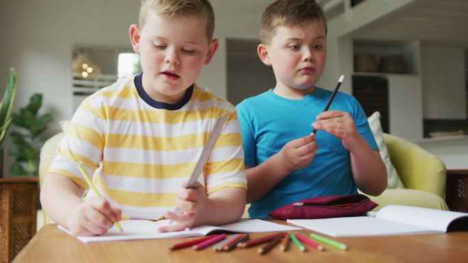 一个白人男孩和他的兄弟坐在桌子旁，在家里学习