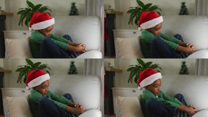 悲伤的非裔美国男孩戴着圣诞帽，在圣诞节坐在沙发上