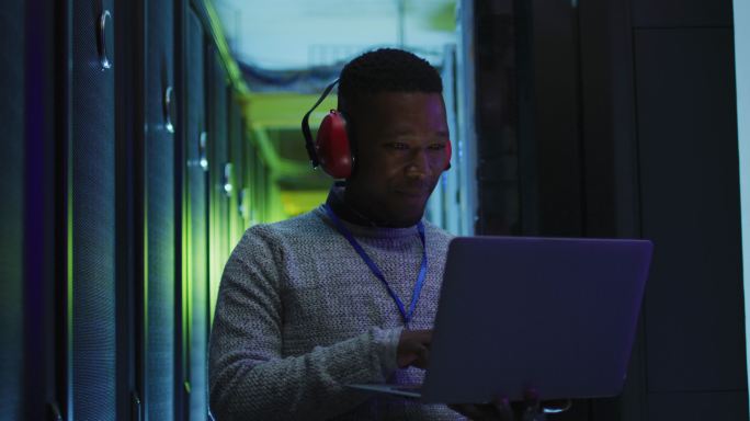 非裔美国男性电脑技术人员使用笔记本电脑在企业服务器室工作