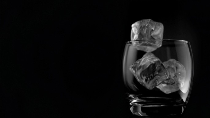 在黑色背景下，冰块以超慢的动作在玻璃杯中下落