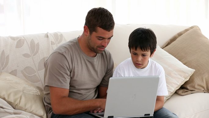 父亲和儿子在沙发上看电脑特学